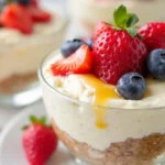 A vibrant cottage cheese dessert topped with fresh berries, honey drizzle, and mint garnish in a glass bowl.