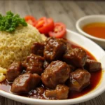 A steaming plate of beef pares served with garlic fried rice and soup, garnished with green onions.