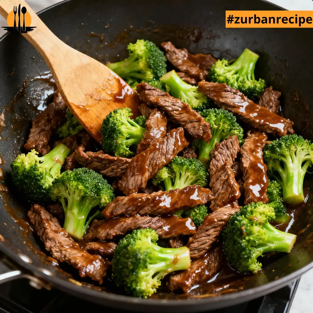 Beef and broccoli coated in glossy stir fry sauce being mixed with a wooden spatula in a hot wok.