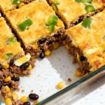 A golden-brown budget-friendly protein bake with melted cheddar cheese, ground pork, and black beans in a glass dish.